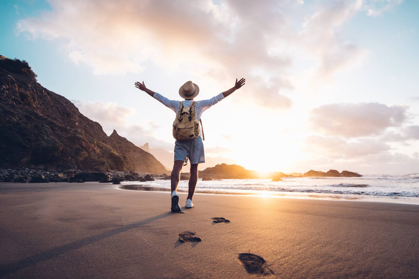 a person standing on a beach with their arms outstretched facing the sun
