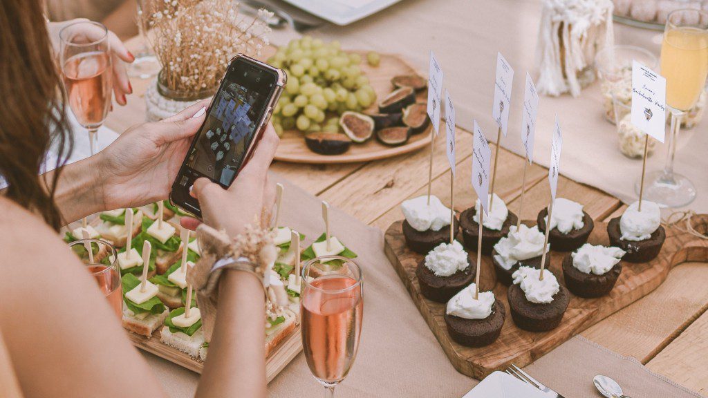 A woman taking a photo of a table full of food and drinks.
