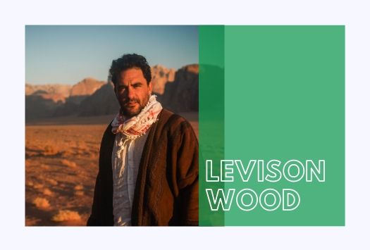 Levison Wood looking into the camera while standing in a deserted area with mountains in the background