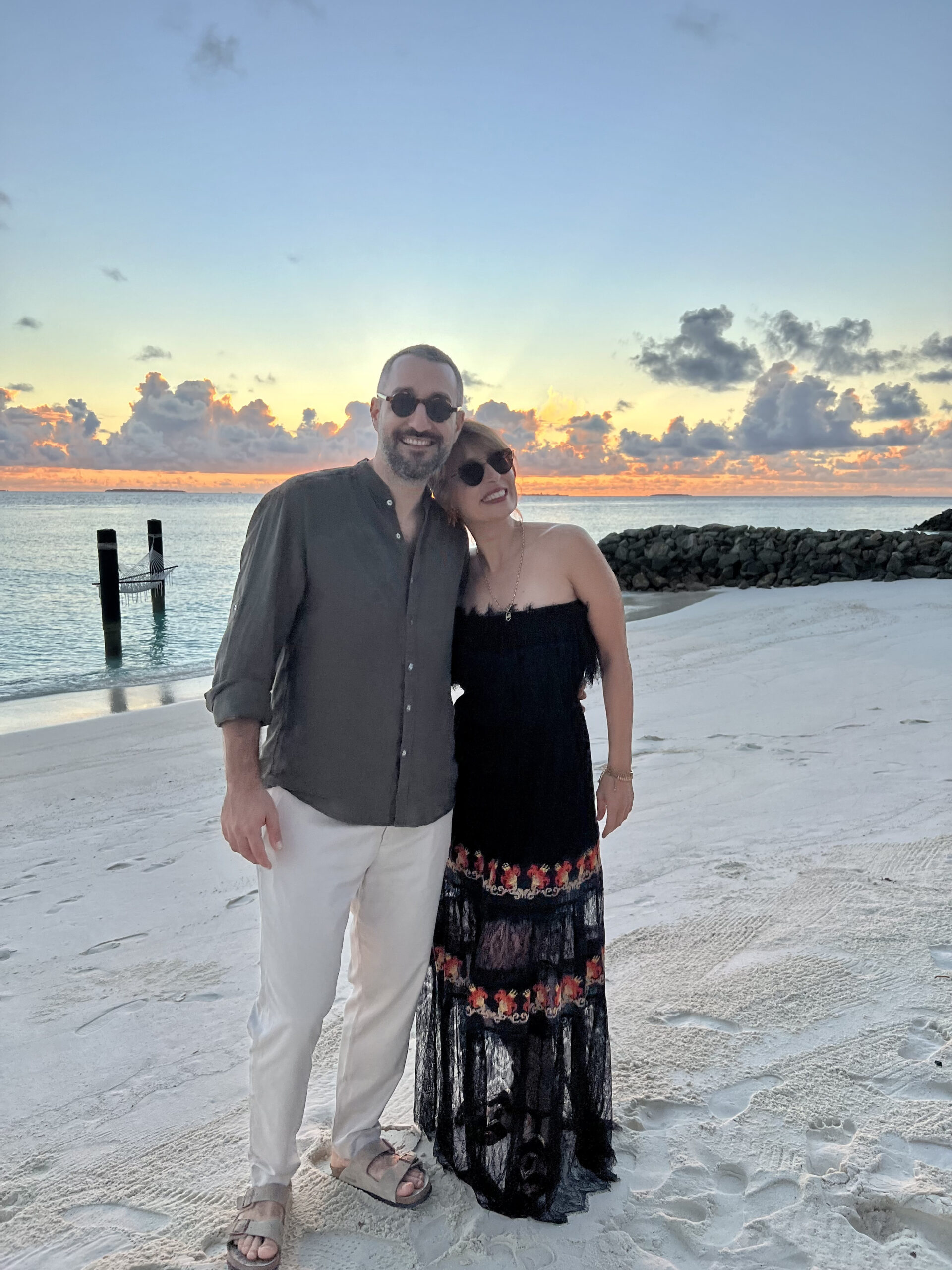 Sinan Sokmen and a lady standing on a sandy beach in the sunset