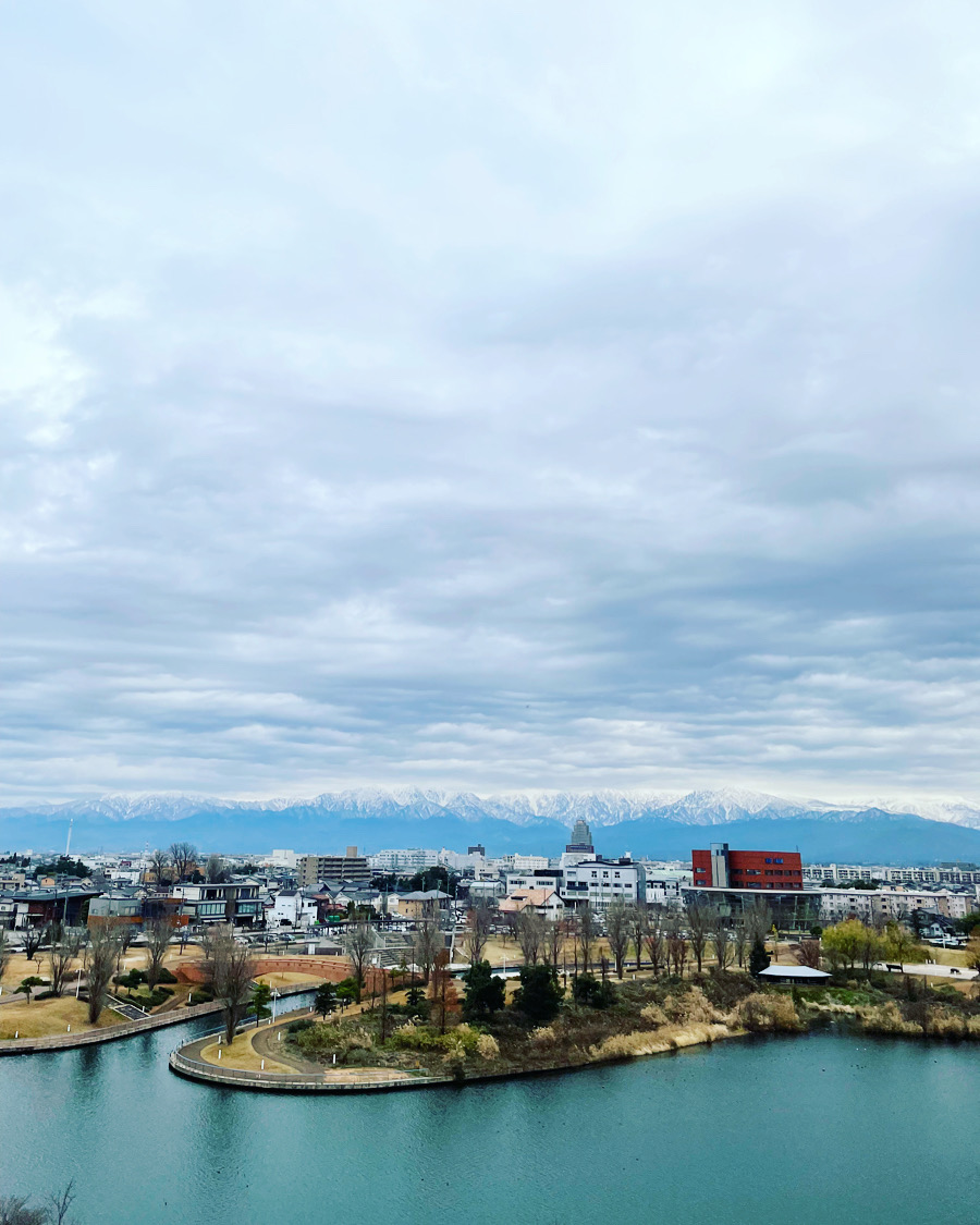 Toyama City with a lake in the foreground and snowy mountains on the back on a cloudy day