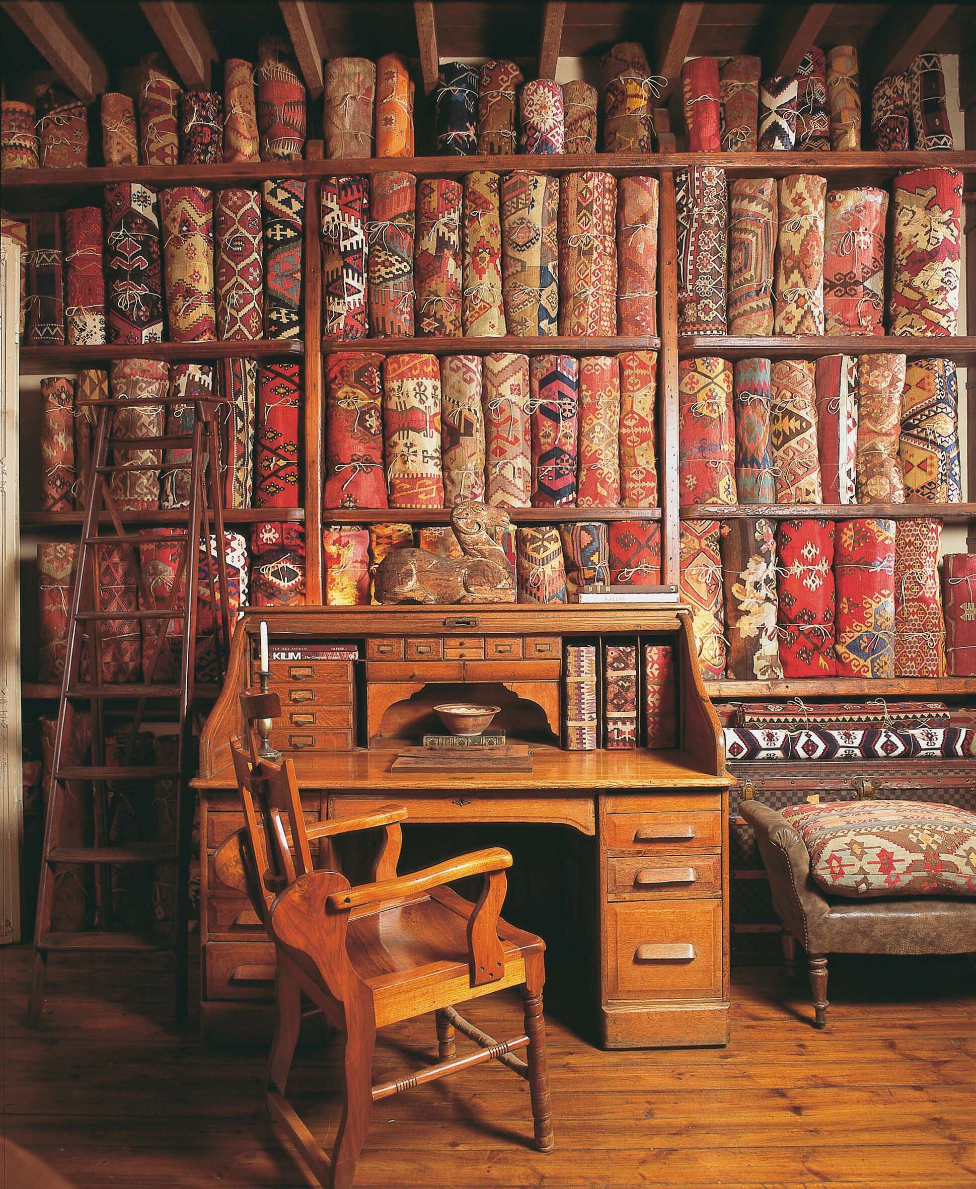 Rolls of carpets are placed on top of each other in Alaturca shop with a wooden table and chair in the foreground