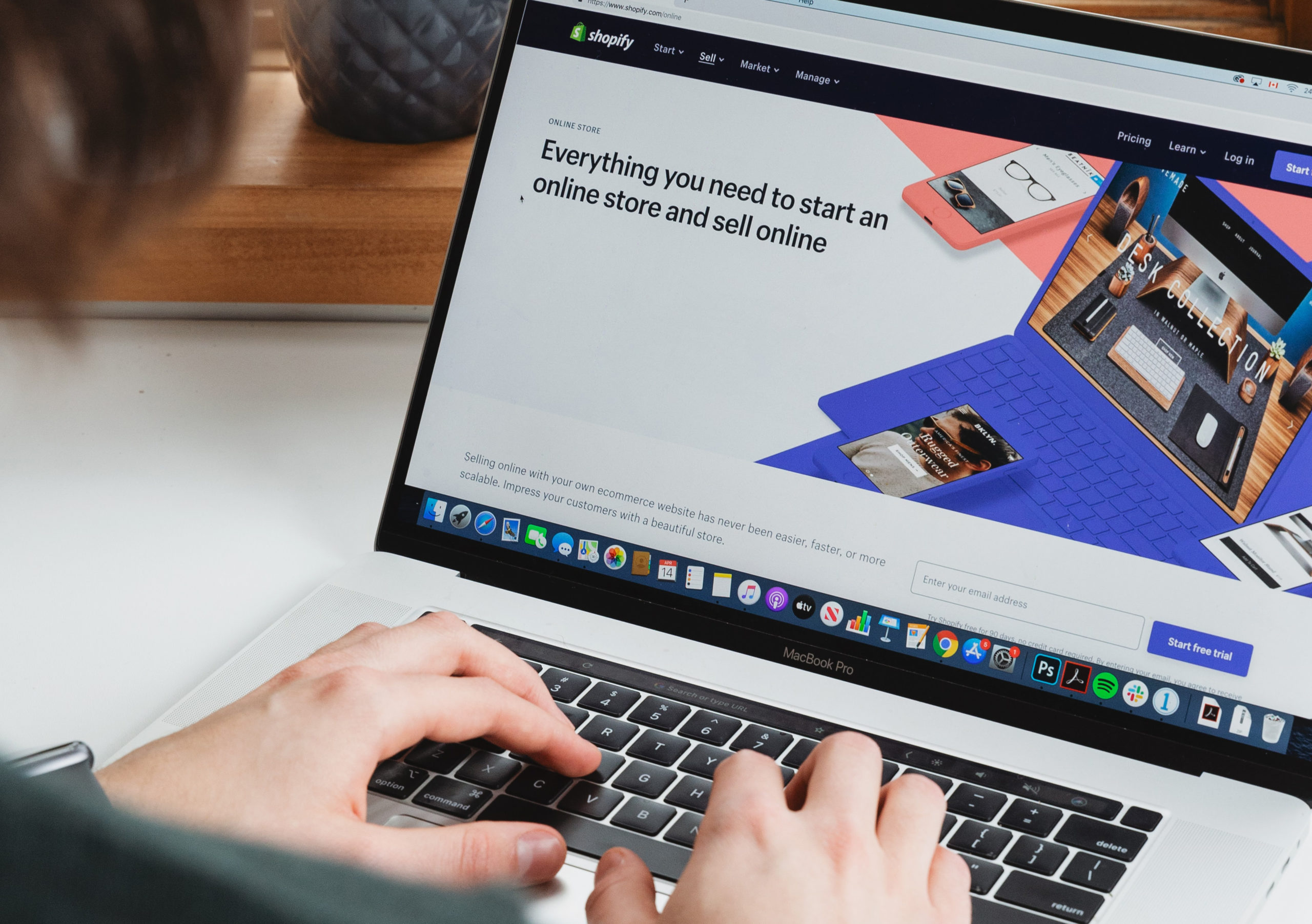 A person using a MacBook Pro displaying Shopify's homepage