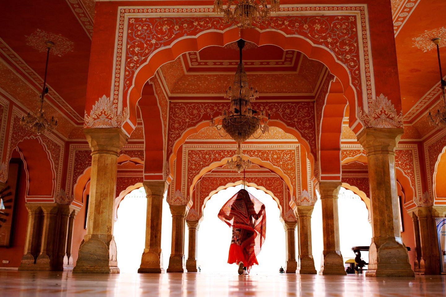 a young Indian woman wearing a red sari walking through an ornate hall