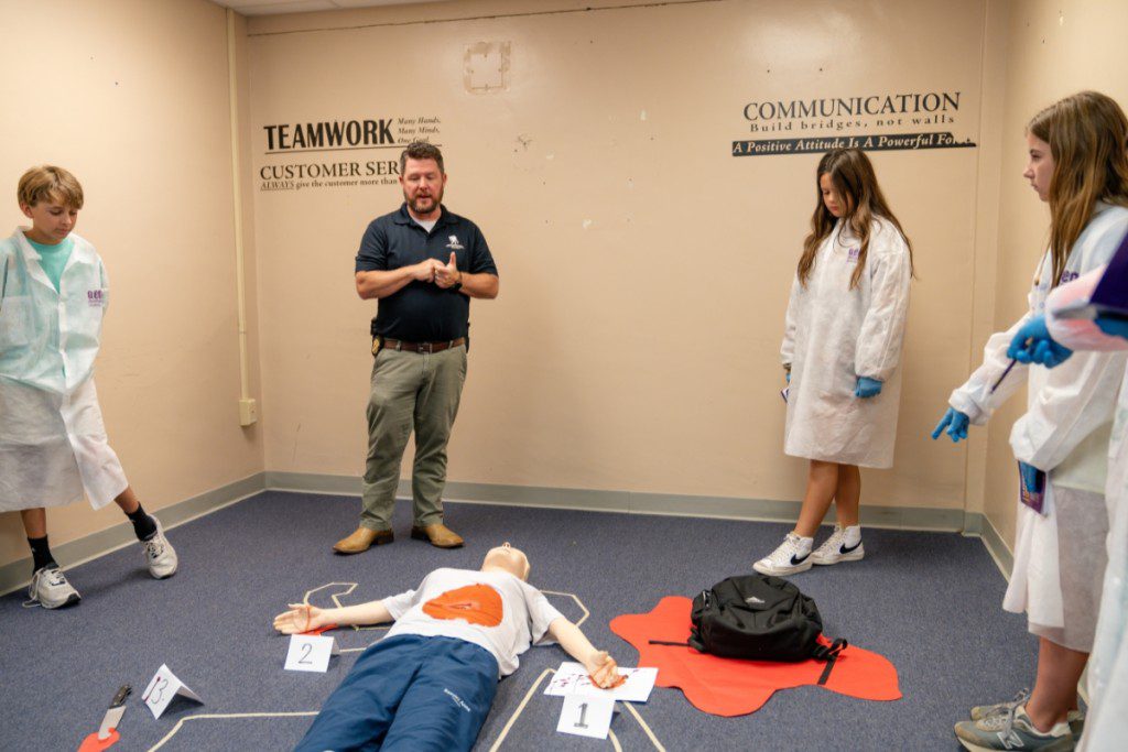 a group of people in white lab coats standing around a dummy