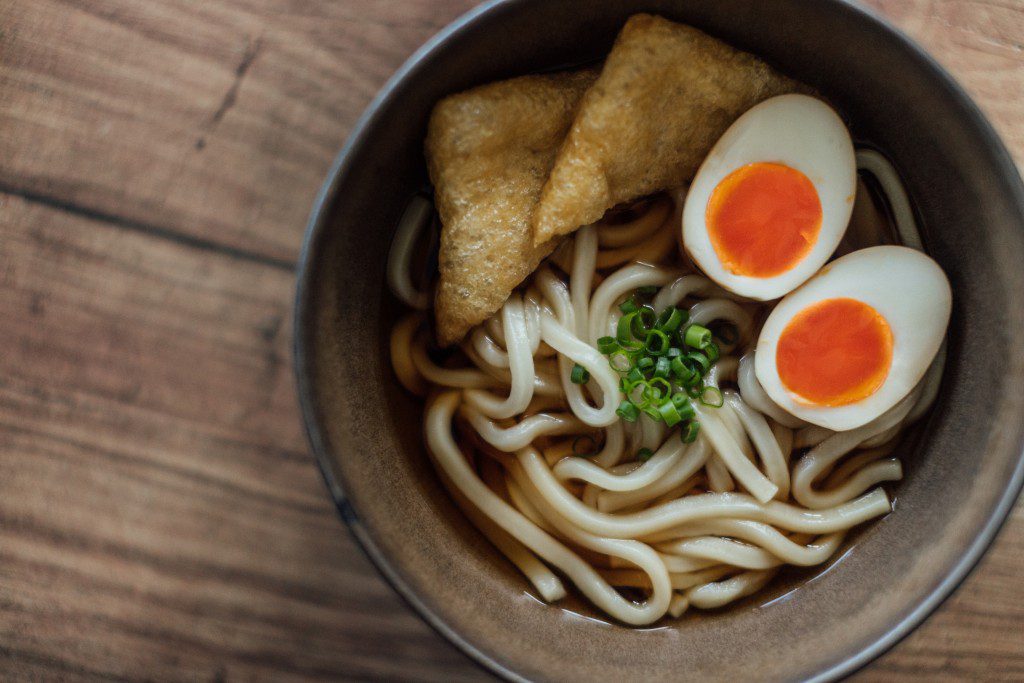 Close-up shot of a bowl of traditional Japanese udon noodles with soft boiled eggs and bean curd served on the dining table.