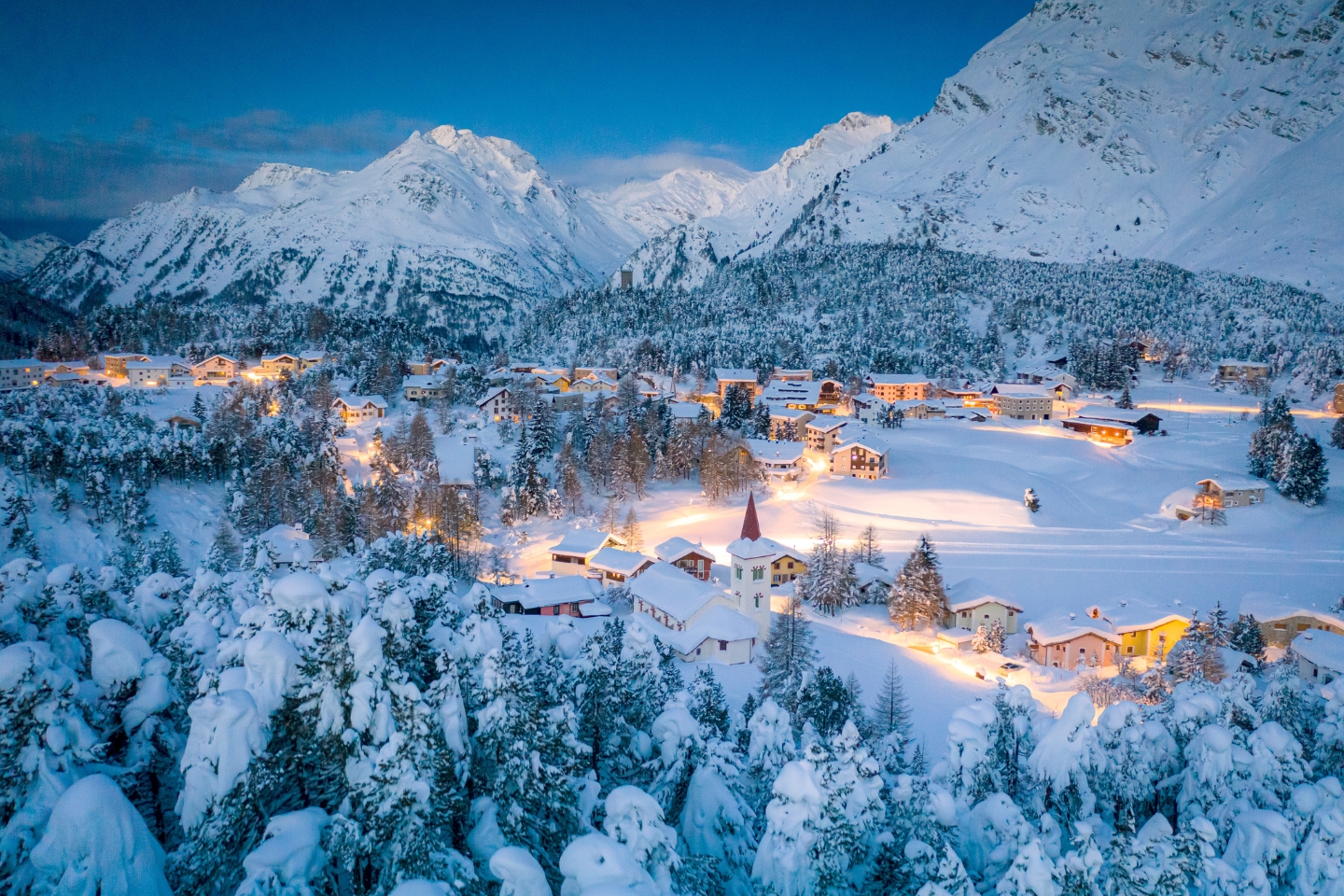 an aerial view of a village in the mountains covered in snow