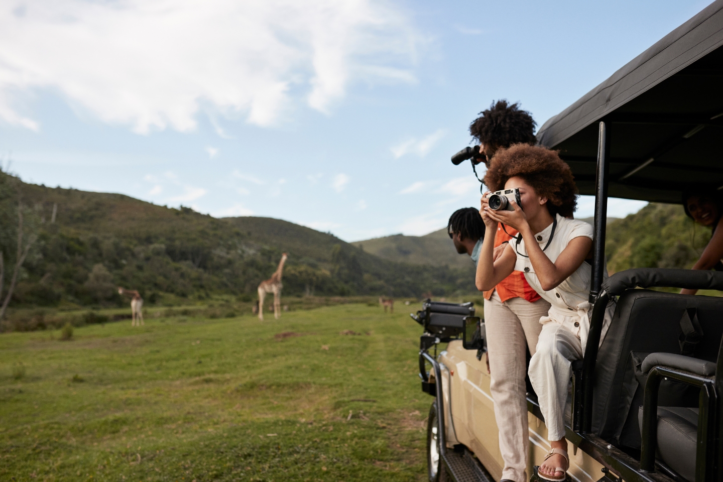 two people taking pictures of giraffes on a safari vehicle