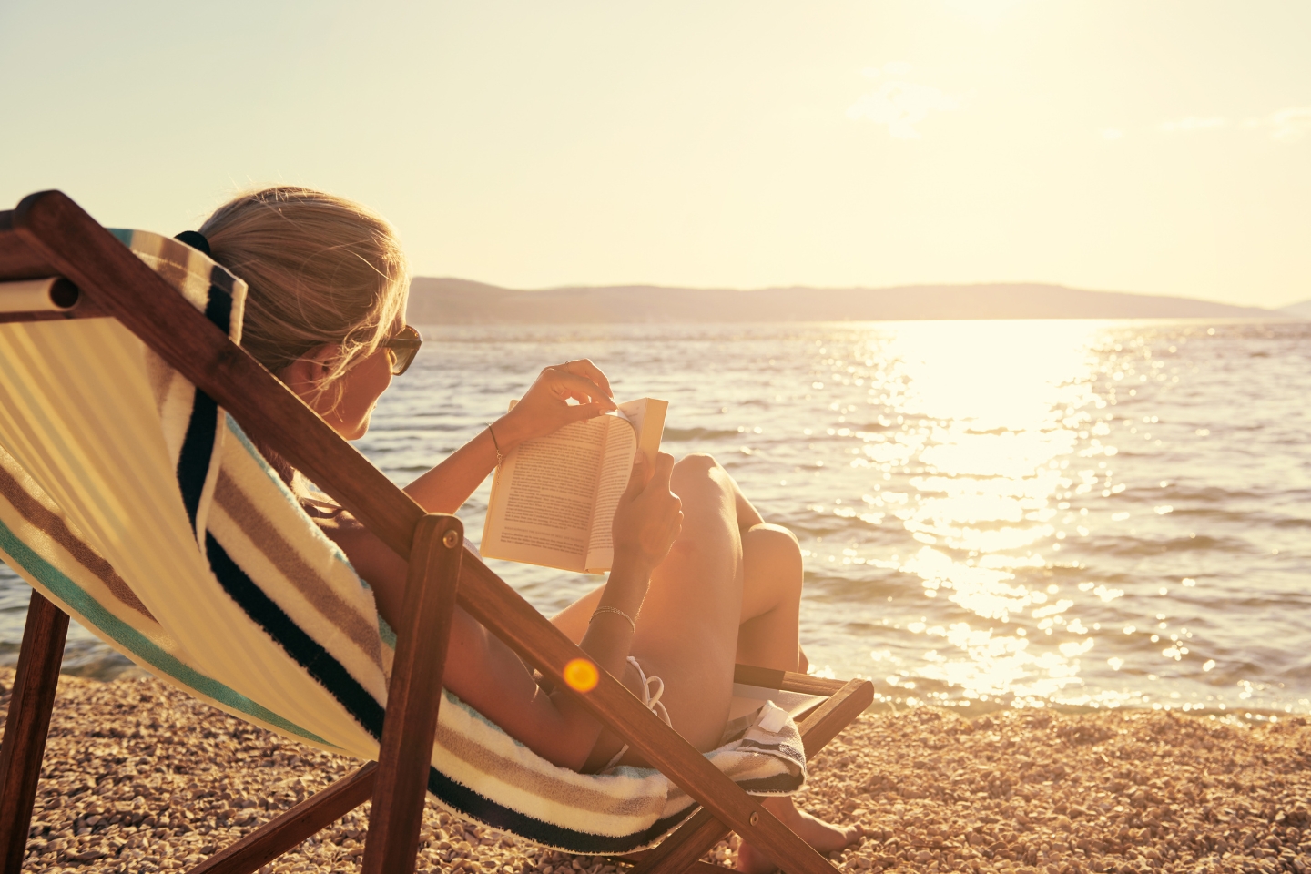 a person reading a book on the beach at sunset