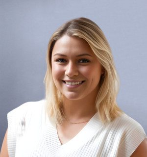 a photo of Nikki D'Amato, a blond person smiling with gray background