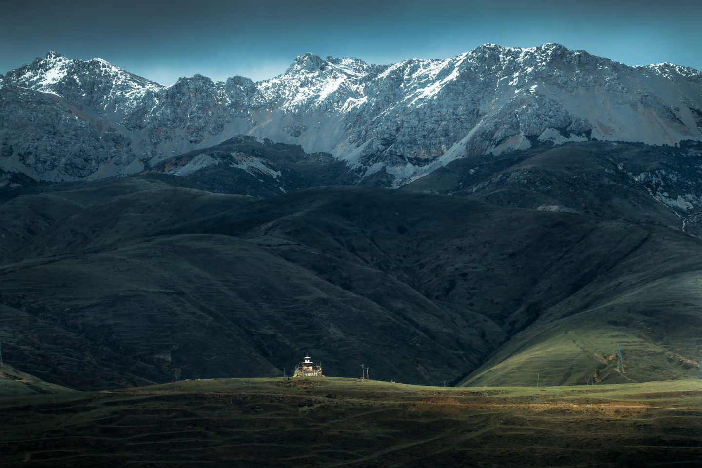 a lone building sits on top of a hill with snow capped mountains in the background