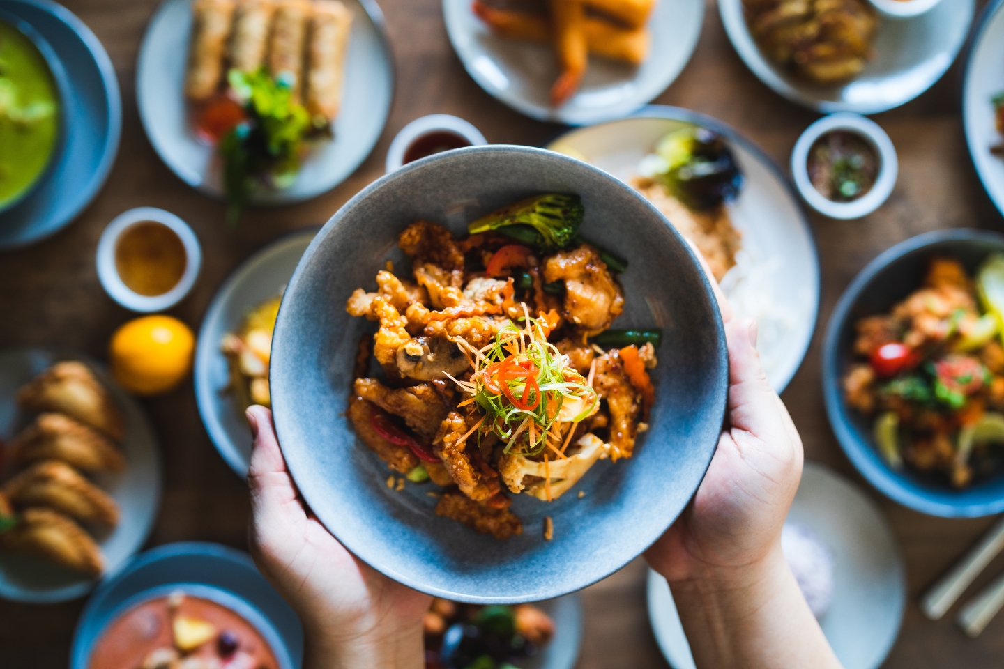 a person holding a bowl full of asian food on a table