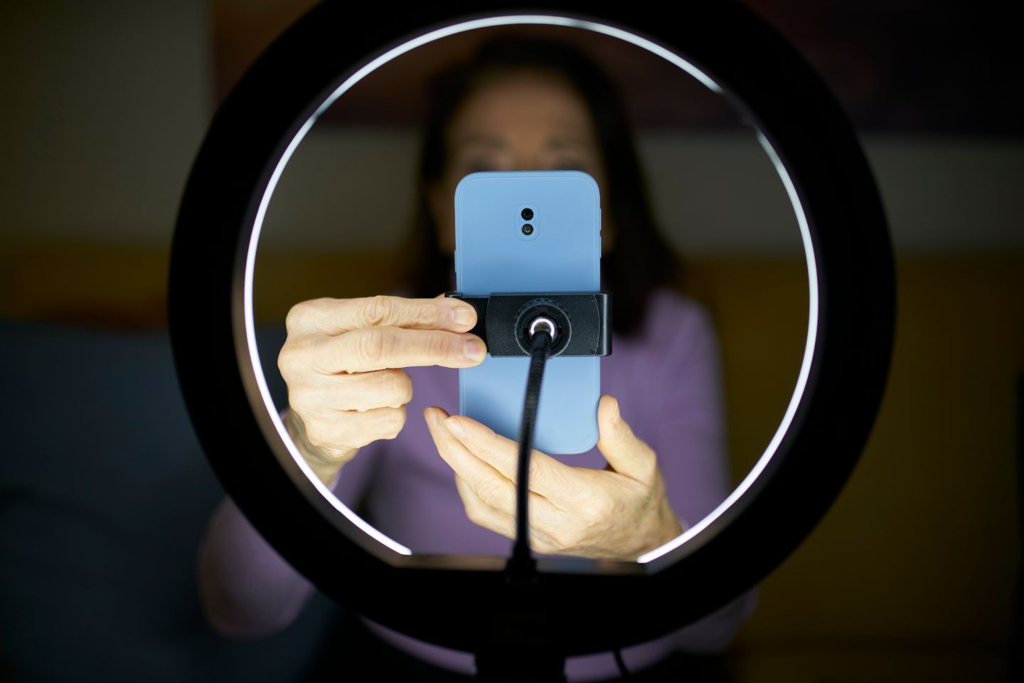 A person holds a light blue smartphone in a ring light, adjusting it for filming or photography.